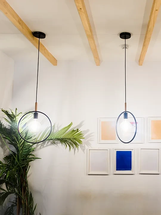 Czarne lampy sufitowe z żarówką w okręgu, wiszące nad jasną przestrzenią z obrazami i roślinami – styl industrialny